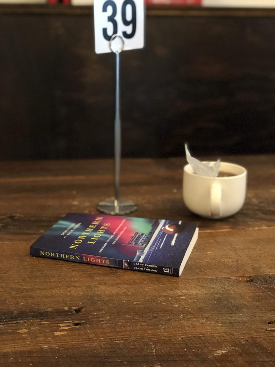 Northern Lights book on a table with a drink and a sign with "39" written on it.
